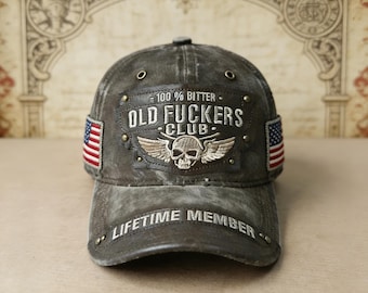 Puede incluir: Gorra de béisbol gris desgastada con el texto "100% Bitter" y "Old Fuckers Club" sobre un emblema de calavera y alas. Cuenta con parches de la bandera estadounidense en los laterales y "Lifetime Member" en la visera. Un accesorio robusto de estilo vintage.