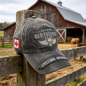 Puede incluir: Gorra de béisbol gris desgastada con el texto "100% Bitter Old Fuckers Club" y una calavera con alas. La gorra también presenta un parche de la bandera canadiense y las palabras "Lifetime Member".