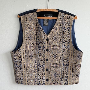 May include: A vintage vest with a navy blue and gold floral pattern. The vest has a V-neck, black buttons, and a navy blue lining. The shoulders are black. The label reads "Liz Claiborne".