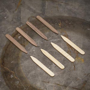 May include: A set of ten wooden collar stays, five are light brown and five are natural wood colour. The stays are arranged in a row on a textured surface.