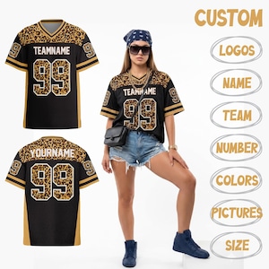 Könnte beinhalten: Ein schwarzes V-Ausschnitt-Trikot mit Leopardenmuster an Schultern und Ärmeln, das den Text TEAMNAME und die Nummer 99 in Weiß zeigt. Das Trikot hat goldene Streifen an den Ärmeln und wird neben Textoptionen für benutzerdefinierte Logos, Namen, Team, Nummer, Farben, Bilder und Größe angezeigt.