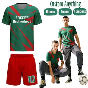 Puede incluir: Conjunto de camiseta y pantalón corto de fútbol verde y rojo. La camiseta tiene el texto "SOCCER Brotherhood" y un diseño diagonal rojo. El pantalón corto es rojo con el número "10" en verde. La imagen también muestra un balón de fútbol y el texto "Custom Anything".