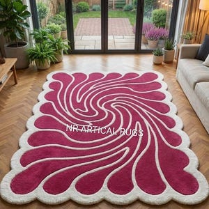 May include: A rectangular area rug with a scalloped edge featuring a deep magenta and white swirling spiral pattern. The rug displays the text NR ARTICAL RUGS in white lettering across the center of the design, set against a wooden floor.