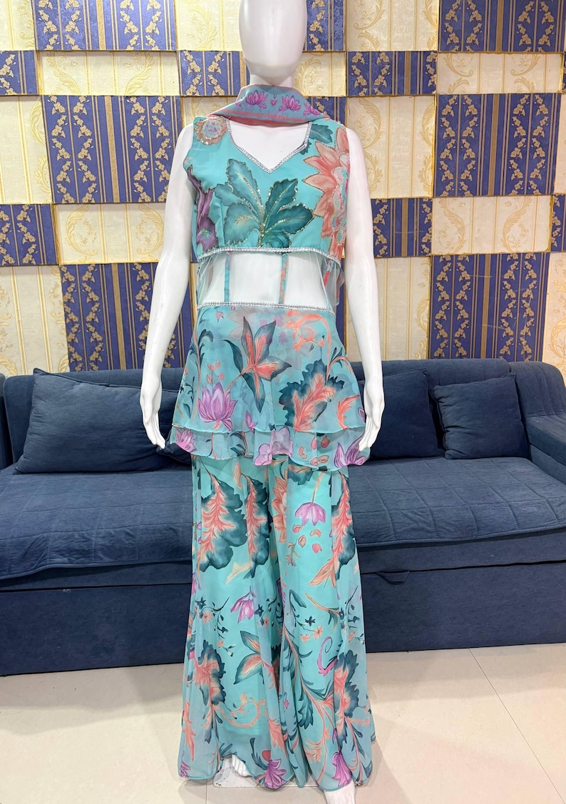 Peut inclure: Une tenue &agrave; imprim&eacute; floral turquoise sur un mannequin. La tenue comprend un haut sans manches avec un col en V, un milieu du corps transparent et un basque &agrave; volants. Un pantalon large assorti et une &eacute;charpe compl&egrave;tent l'ensemble. Le motif floral pr&eacute;sente des accents roses, oranges et verts.