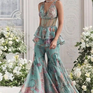 Peut inclure: Ensemble deux pi&egrave;ces de c&eacute;r&eacute;monie vert d'eau. Le haut sans manches a un d&eacute;collet&eacute; plongeant et une taille p&eacute;plum, associ&eacute; &agrave; un pantalon &agrave; jambes larges. Le motif floral comprend des teintes roses et violettes, cr&eacute;ant un look &eacute;l&eacute;gant.