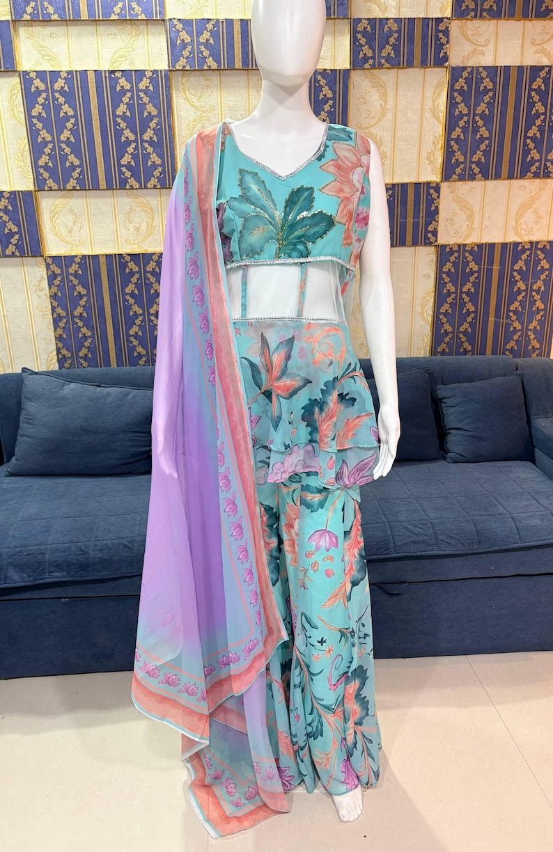 Peut inclure: Une tenue &agrave; imprim&eacute; floral turquoise sur un mannequin. La tenue comprend un haut sans manches avec un col en V, un haut de style p&eacute;plum et un pantalon large. Une &eacute;charpe transparente lavande avec une bordure florale est drap&eacute;e sur la tenue. Le fond pr&eacute;sente un canap&eacute; bleu et un mur &agrave; motifs.
