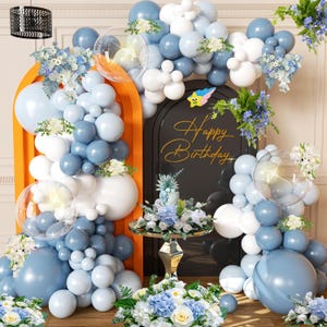 May include: A festive birthday party scene with blue, white, and clear balloons, floral arrangements, and a gold "Happy Birthday" sign. The balloons are arranged in arches and clusters, creating a celebratory atmosphere.