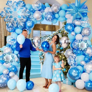 May include: A festive winter-themed balloon arch in shades of blue, silver, and white, featuring snowflake and star-shaped balloons. A family poses with balloons in front of the arch, creating a celebratory atmosphere.