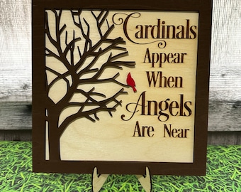 May include: A wooden sign with a brown frame and a cutout of a tree with a red cardinal perched on a branch. The sign reads "Cardinals Appear When Angels Are Near".