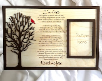 May include: Wooden memorial picture frame with a laser-cut tree and a red bird. The frame includes a poem titled "I'm Free" and a space to insert a picture. The frame is made of light-colored wood with a dark brown border.