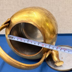 以下が含まれることがあります： 蓋、ハンドル、注ぎ口が付いたヴィンテージの真鍮製ティーポット。ティーポットは装飾的なデザインで、直径は約10cmです。 ティーポットの中にはメジャーがあります。
