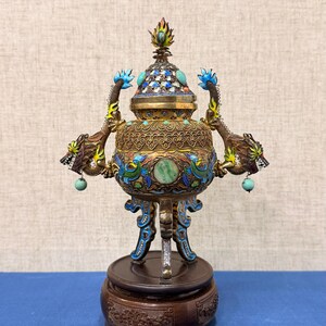 May include: An ornate antique bronze incense burner with intricate dragon and floral designs. Features turquoise and jewel accents, a wooden base, and a detailed lid. A decorative piece.