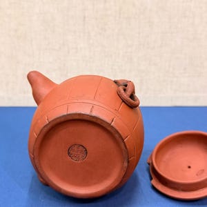 以下が含まれることがあります： 樽のような形と別蓋の小さな赤茶色の陶器のティーポット。 ティーポットには注ぎ口、取っ手、装飾的なデザインがあります。 蓋は丸く、ぴったりと収まります。 ティーポットはおそらくお茶を淹れるために使用されます。