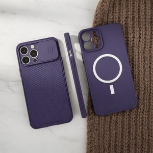 May include: Three purple phone cases. Two cases are shown with a textured back and camera lens protection. One case has a white circle and a dash symbol. The cases are on a brown knitted surface.