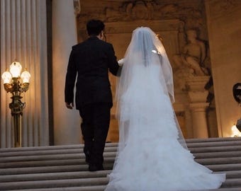 May include: A bride and groom walking down a grand staircase in a white wedding dress and a black suit.