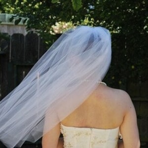 May include: A white tulle bridal veil with a single layer and a scalloped edge. The veil is flowing in the wind.