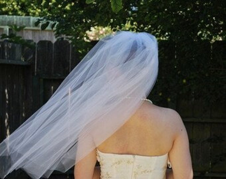 May include: A white tulle bridal veil with a single layer and a scalloped edge. The veil is flowing in the wind.