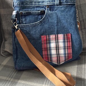 Könnte beinhalten: Eine Jeans-Umhängetasche mit einer karierten Tasche. Die Tasche besteht aus blauem Jeansstoff und hat einen braunen Riemen. Die karierte Tasche hat rote, weiße und schwarze Farben.