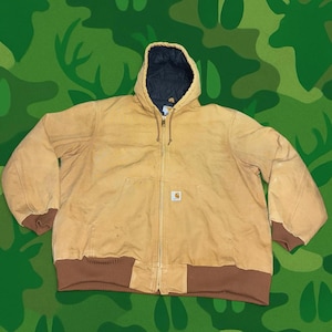 May include: A tan Carhartt hooded jacket with a black interior lining. The jacket features a full-length zipper, a brown ribbed hem and cuffs, and a small square logo on the front pocket. The hood has a drawstring closure.