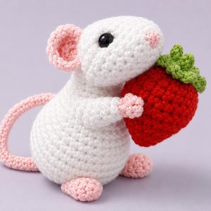 May include: A white crocheted mouse toy with pink inner ears, pink feet, and a pink tail, holding a bright red crocheted strawberry with a green leafy top. The mouse has small black bead eyes and a tiny pink stitched nose, crafted in yarn.