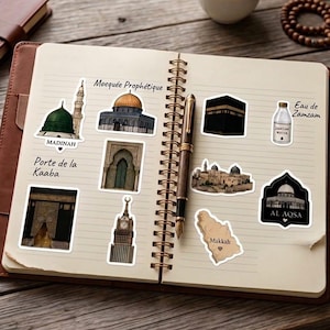 Peut inclure: Un carnet ouvert avec des autocollants de monuments islamiques, dont la Kaaba et la mosquée du Prophète. Les autocollants sont sur une page lignée, à côté d'un stylo. Une tasse de thé et un chapelet sont également visibles.