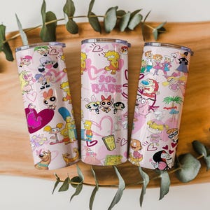 May include: Three pink insulated tumblers decorated with 1990s cartoon characters. The tumblers have a pink background with various cartoon characters, hearts, and the text "90s BABES". Each tumbler has a silver lid.