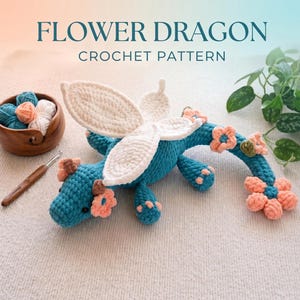 Peut inclure: Un dragon bleu crocheté avec des ailes blanches et des fleurs pêche. Le texte "FLOWER DRAGON CROCHET PATTERN" est affiché en haut de l'image. Un bol en bois de fil et un crochet sont également visibles.
