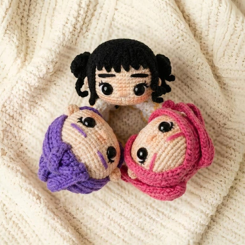 May include: Three handmade crochet doll heads. One doll has black hair in pigtails, and the other two have purple and pink head coverings. The dolls have black eyes and are made with beige and white yarn.