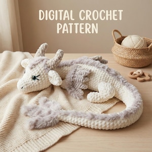 Op de afbeelding: Een gehaakte draak in wit en grijs, met een pluizige staart en accenten. De draak ligt op een crèmekleurige deken. De tekst "DIGITAL CROCHET PATTERN" staat bovenaan de afbeelding.