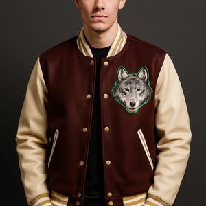 Puede incluir: Chaqueta universitaria granate y crema con un parche de lobo. La chaqueta tiene mangas color crema, botones dorados y detalles a rayas en los puños y el cuello. El parche del lobo es verde y gris.