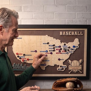 May include: A wooden wall map of the United States featuring the text BASEBALL MAJOR LEAGUE and Michael Family Stadium Map. The map includes various colored circular markers placed on specific locations and a brown leather baseball glove with a ball.