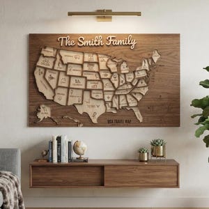 May include: A rectangular wooden wall map of the United States featuring a 3D layered design with state borders and engraved icons. The text "The Smith Family" is displayed in large script at the top, with "USA TRAVEL MAP" printed at the bottom.