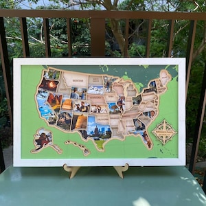 Puede incluir: Un mapa mural rectangular de los Estados Unidos en un marco blanco sobre un fondo verde claro. El mapa se compone de recortes de madera con forma de estados, cada uno relleno con una fotografía. Una rosa de los vientos de madera incluye el texto Robinson's Family.