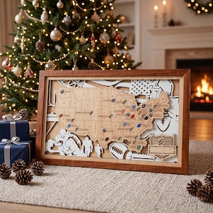 May include: A framed wooden map of the United States featuring laser-cut state borders and small football-shaped markers placed across various locations. The design includes white layered silhouettes of football players and a shield-shaped emblem.