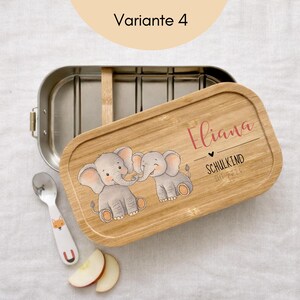 May include: A rectangular stainless steel lunch box with a bamboo lid featuring two illustrated elephants, the name Eliana, and the text SCHULKIND SEIT 2026. A small silver spoon with a fox graphic and two apple slices are placed nearby.