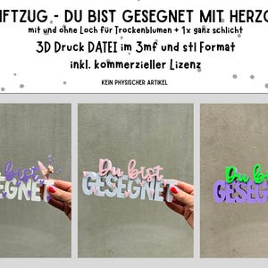 Könnte beinhalten: Ein 3D-gedrucktes Schild mit dem deutschen Satz "Du bist GESEGNET" (Du bist gesegnet) in Weiß, mit den Worten in Lila, Rosa und Grün. Das Schild enthält Herzakzente und wird von einer Person hochgehalten.