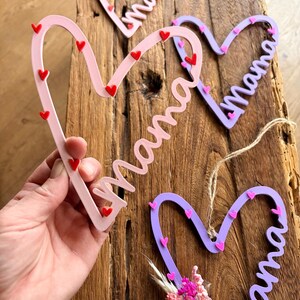 May include: Pink, lilac, and red heart-shaped decorations with the word "Mama" in cursive. Each heart is decorated with small heart accents. One heart has a small bouquet of pink flowers.
