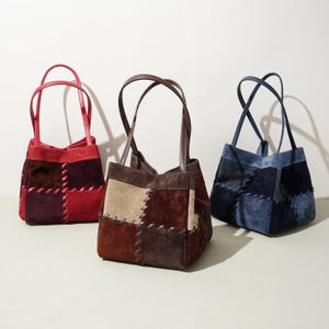 May include: Three suede tote bags in red, brown, and blue. Each bag features a patchwork design with contrasting stitching and matching handles. The bags are small, with a structured shape, and are suitable for everyday use.