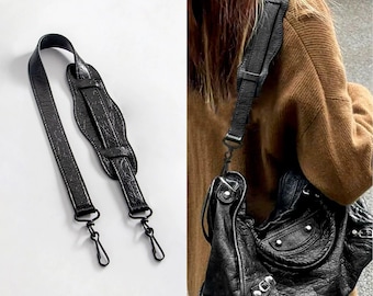 May include: A black textured leather shoulder strap featuring a contoured shoulder pad and two metal swivel lobster claw clasps at the ends. The strap is shown detached and also attached to a black leather handbag with silver metal hardware.