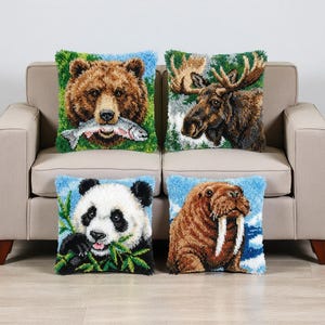 Puede incluir: Cuatro cojines cuadrados con diseños de animales. Los cojines presentan un oso con un pez, un alce, un panda comiendo bambú y una morsa. Cada cojín tiene un borde azul y un fondo verde.