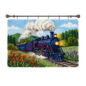 May include: A latch hook wall hanging featuring a blue steam locomotive travelling through a landscape with green trees, red flowers, and purple blossoms. The train emits white smoke and has bright yellow lights, all suspended from a metal rod.
