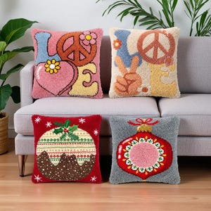 May include: Four square throw pillows with textured punch needle designs. The top left features the word LOVE with a peace sign and heart. The top right shows a peace sign hand gesture. The bottom left is a Christmas pudding, and the bottom right is a holiday ornament.