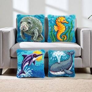 May include: Four square throw pillows with sea creature designs. The pillows feature a manatee, seahorse, dolphin, and whale, all against a blue background. The pillows are placed on a gray couch.