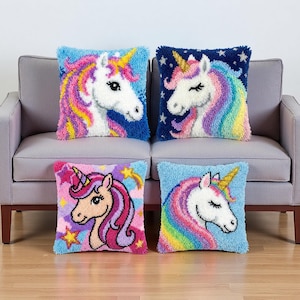 May include: Four square throw pillows with unicorn designs. Each pillow features a different unicorn with a white face, colorful mane, and a golden horn. The backgrounds are various shades of blue, pink, and purple, with star accents.