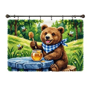May include: A rectangular punch needle wall hanging featuring a brown bear wearing a blue and white checkered bandana. The bear sits at a blue stump, holding a wooden honey dipper over a glass jar of honey, surrounded by three flying bees.