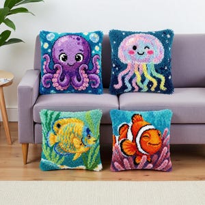 Könnte beinhalten: Vier dekorative Zierkissen mit Designs von Meeresbewohnern. Die Kissen zeigen einen Oktopus, eine Qualle und zwei verschiedene Fische. Jedes Kissen hat ein strukturiertes, getuftetes Aussehen mit leuchtenden Farben, darunter Blau, Lila, Orange und Gelb.
