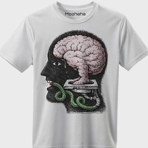 Op de afbeelding: Wit t-shirt met een surrealistische grafische afbeelding. Het ontwerp toont een menselijk profiel met een hersen, een groene slang en de tekst "Moohaha" bij de halslijn. De afbeelding is gedetailleerd en artistiek.