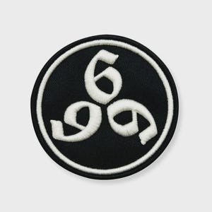 Puede incluir: Un parche redondo negro con un borde blanco. El parche presenta el número "6" repetido tres veces en un diseño estilizado y arremolinado. Los números están en una fuente blanca y en negrita, creando un fuerte contraste con el fondo negro.