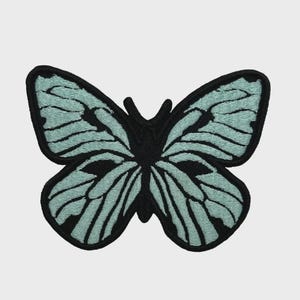Könnte beinhalten: Gestickter Schmetterlingsaufnäher mit schwarzem Umriss und helltürkisem Flügeldesign. Der Schmetterling hat detaillierte Flügelmuster und einen schwarzen Körper. Dieser dekorative Aufnäher kann auf Stoff genäht oder gebügelt werden.