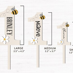 May include: Three wooden number one cake toppers with a bee and flower design. The toppers are available in three sizes: large (2.5 inches by 4.3 inches), medium (2.2 inches by 3.7 inches), and small (1.5 inches by 2.6 inches).